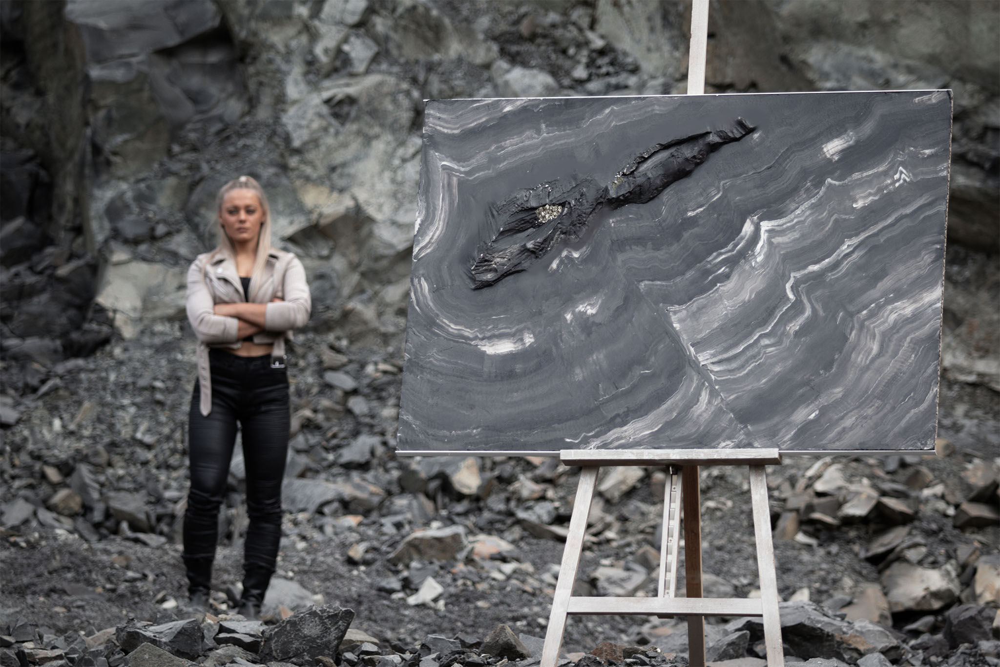 Man sieht ein Kunstwerk von Jennit aus der Serie Marbleous mit Pyrit in ihren corporate colors anthrazit, schwarz und taupe in einem Steinbruch. Die Künstlerin steht im Hintergrund.