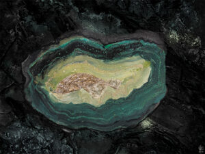 Geode Wall art von Künstlerin Jennit in Smaragdgrün und gold und Quarzmineralien und gemalter Achatgeode in Acrylpouring Technik, umgeben von schwarzen Stein.