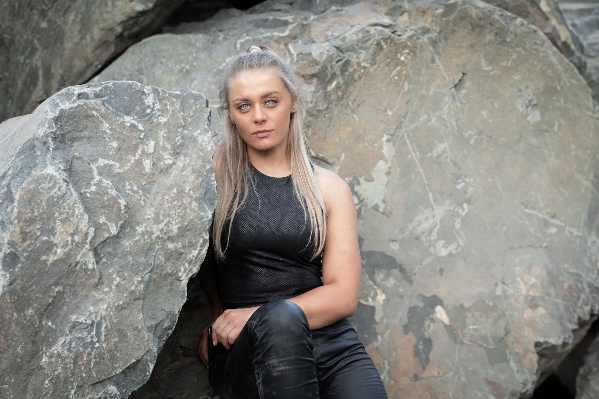 Die Künstlerin Jennit sieht mit entschlossen Blick in die Kamera während sie auf Steinen sitzt.