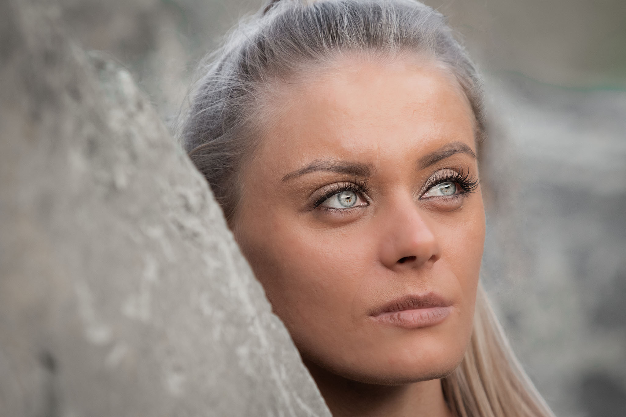 Ein Portrait der Künstlerin Jennit in einem Steinbruch. Ihr Blick ist nachdenklich abgewendet und ihre hellen, blaugrünen Augen stechen heraus.